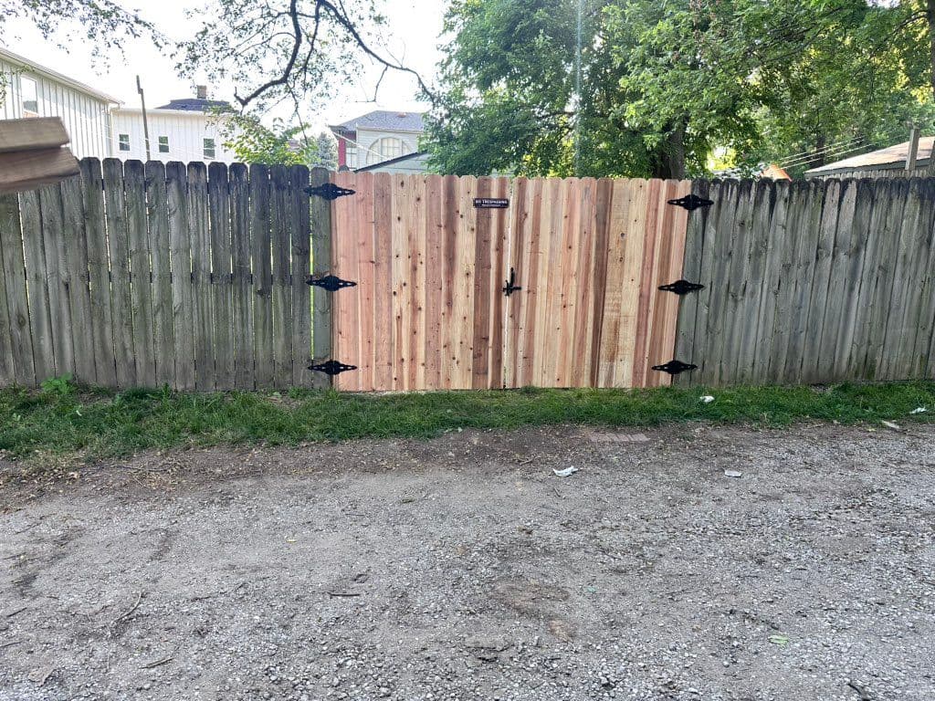 Puerta doble de cedro nueva con bisagras negras instalada en cerca de madera envejecida