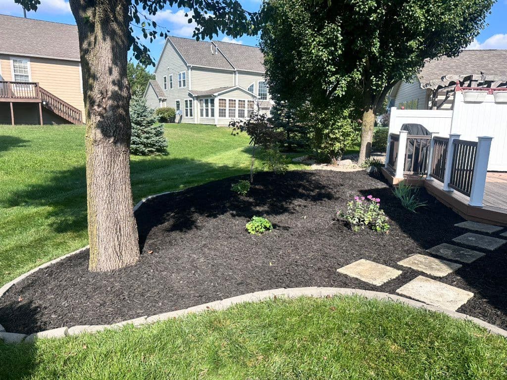 Macizo curvo de mantillo negro con bordillo de piedra y plantas pequeñas junto a terraza