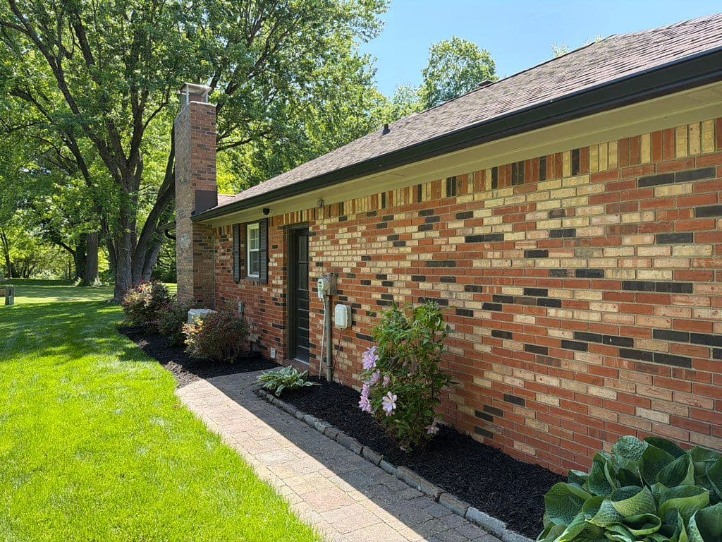 Freshly mulched flower bed along brick house with paver walkway and trimmed shrubs