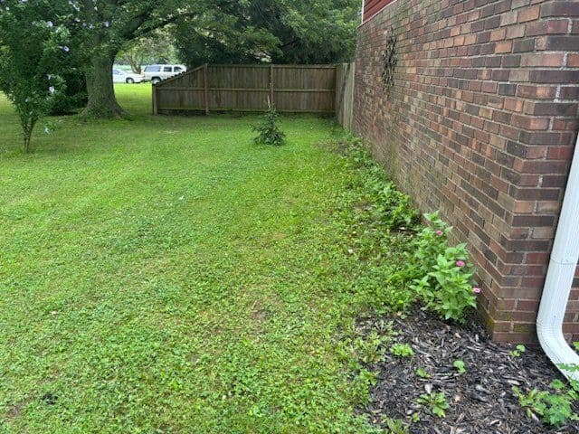 Mulched flower bed along brick house with wood privacy fence behind