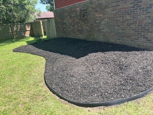 Dark mulch bed with curved plastic edging along brick house exterior