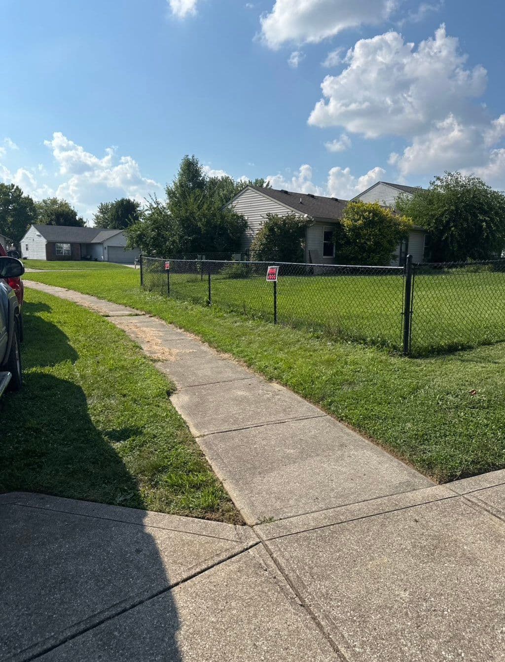 Black chain link fence along sidewalk bordering green residential lawn