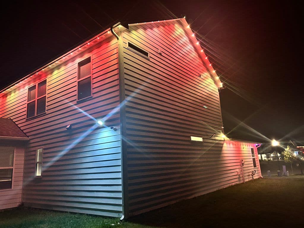 Red string lights installed along roofline of two-story house at night