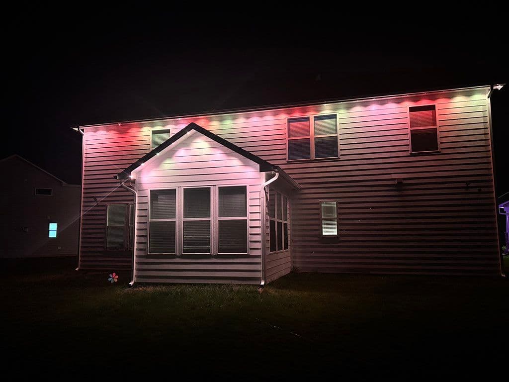 Red and green LED string lights installed along roofline of two-story house at night