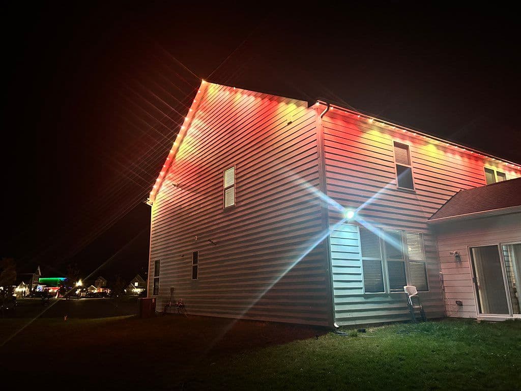 Red and orange LED string lights installed along roofline of two-story house at night