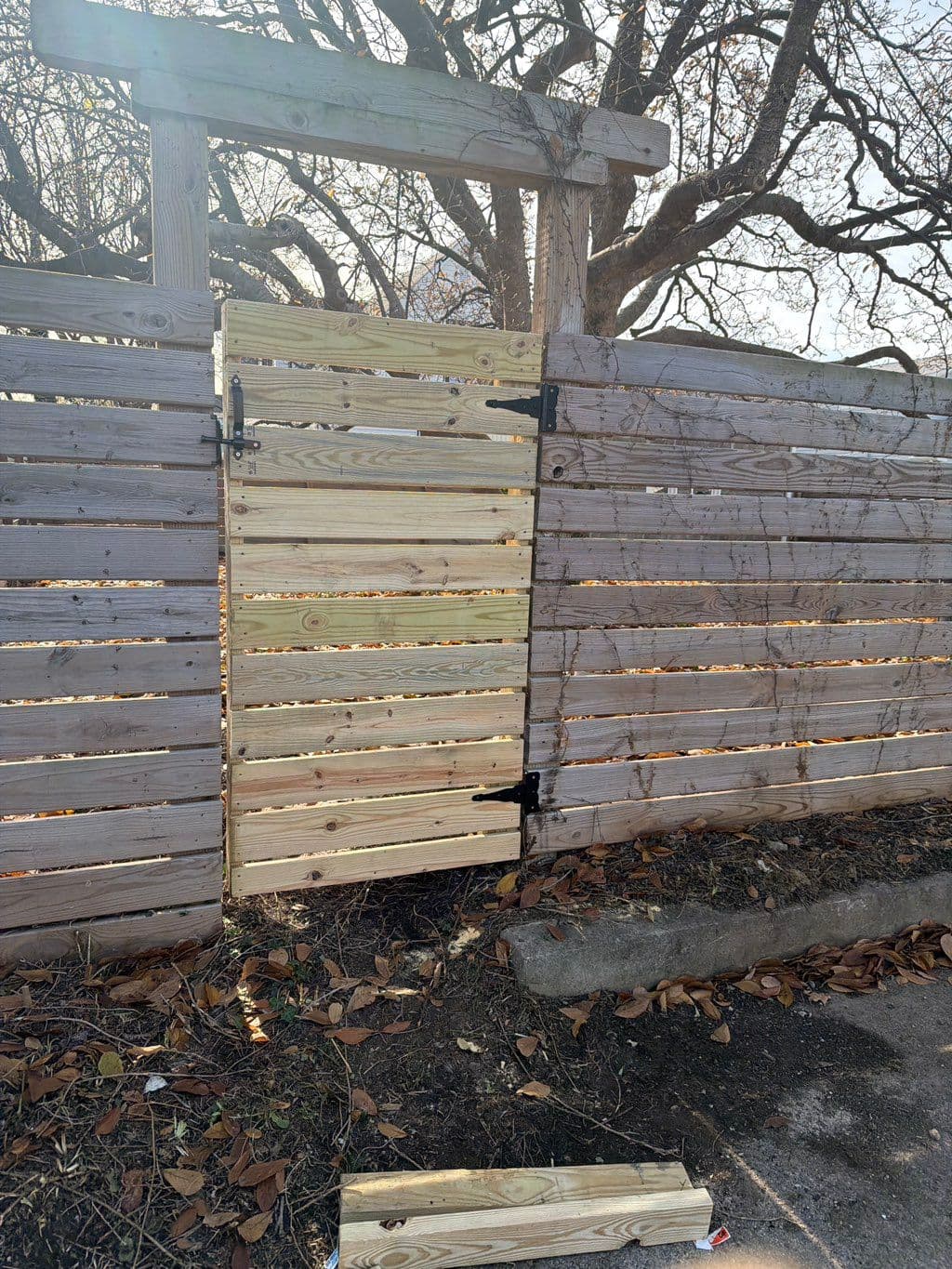 New wood gate with black hinges installed in horizontal slat fence