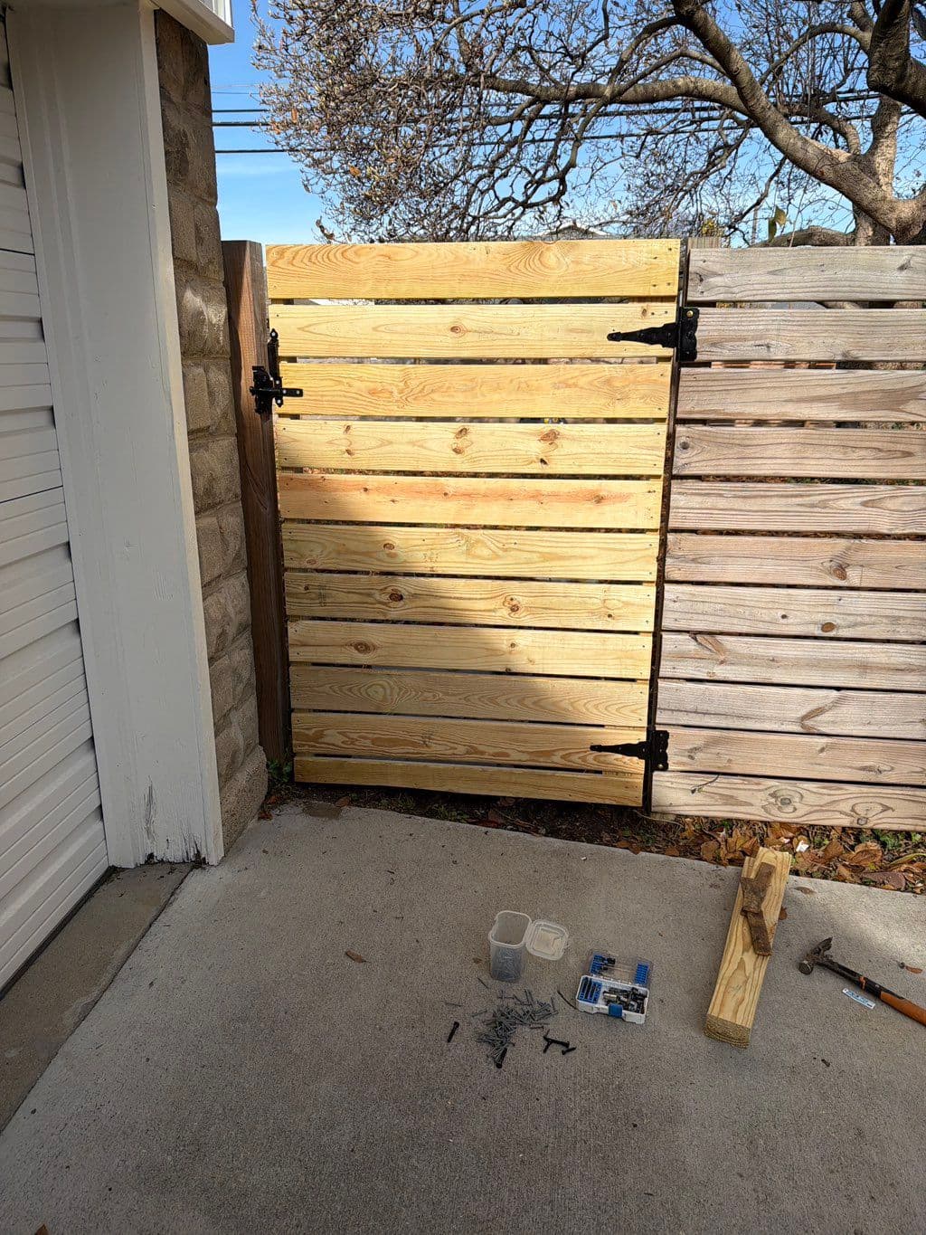 New horizontal wood gate with black hinges beside weathered fence panel