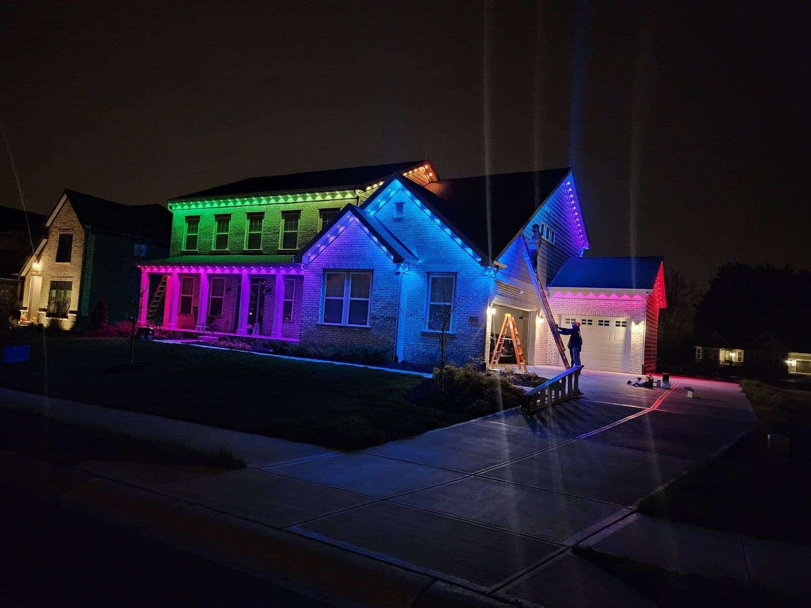 Multicolor LED string lights installed along roofline of brick house at night