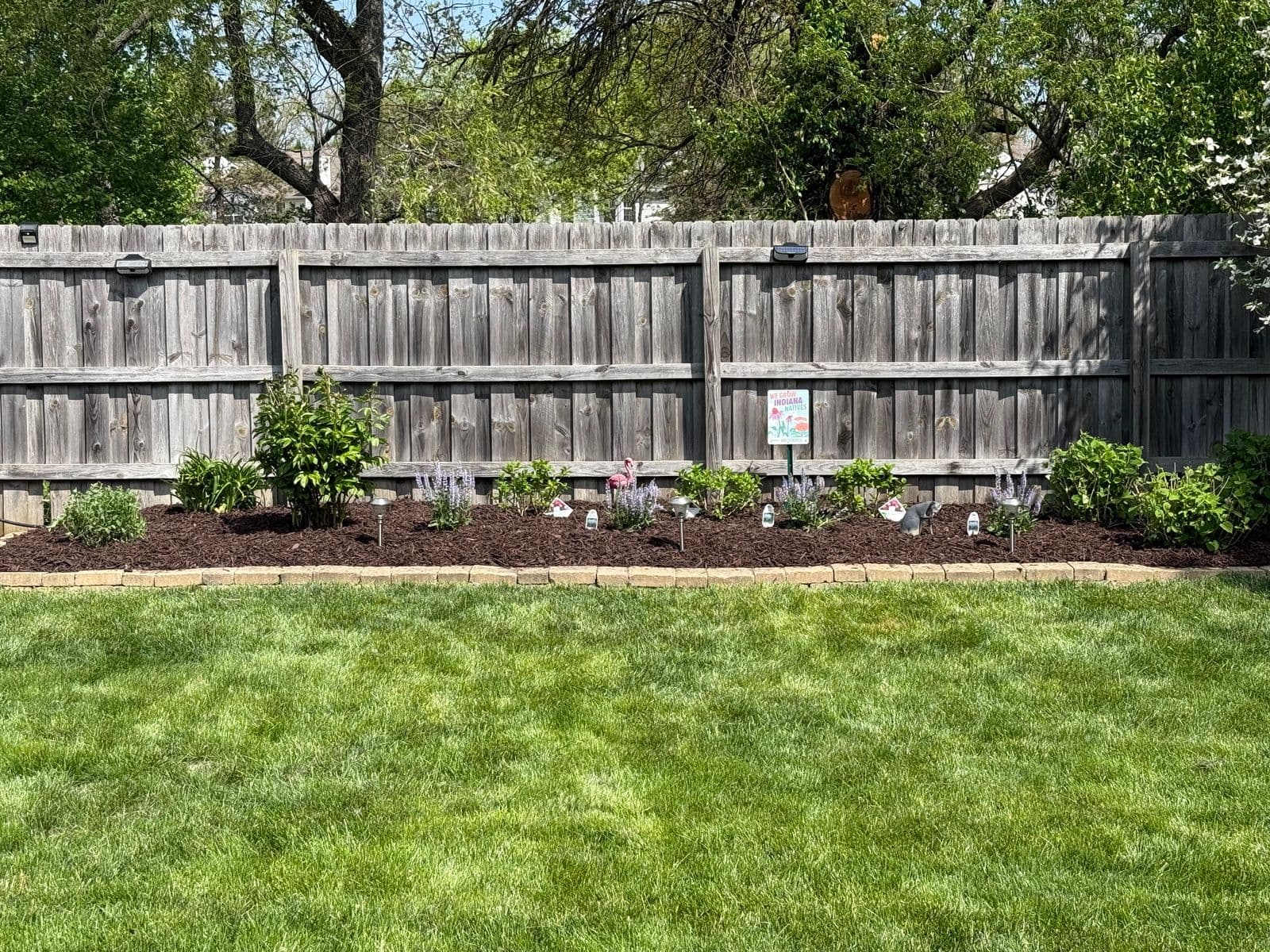 Mulched garden bed with new plantings along weathered wood privacy fence
