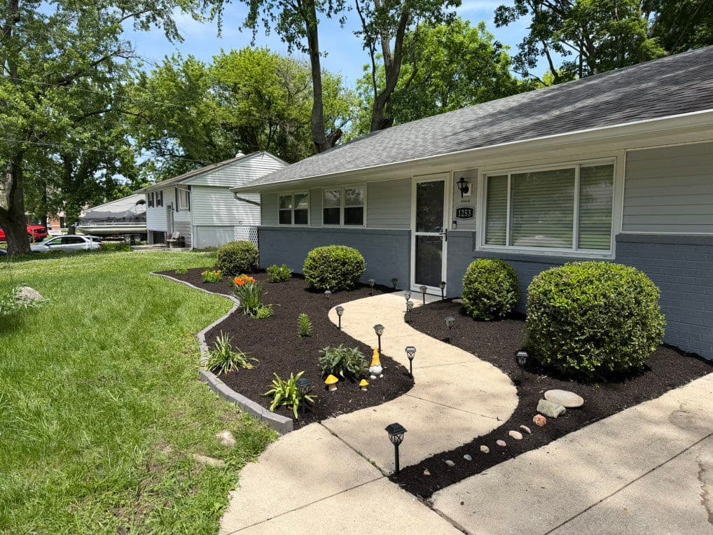 Front yard bed with dark mulch, trimmed shrubs, and solar path lights